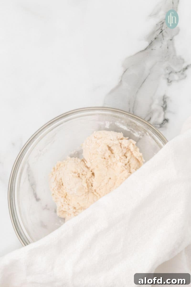 Artisan Sourdough English Muffin Bread 11 A bowl of dough, partially covered with a towel, undergoing its initial rest period.
