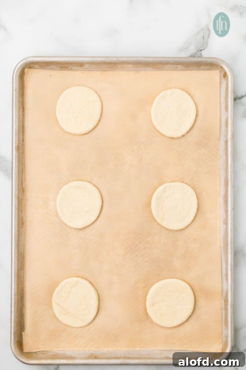 Artisan Sourdough English Muffin Bread 17 A baking sheet lined with parchment paper, holding 6 perfectly round doughs ready for their second rise.
