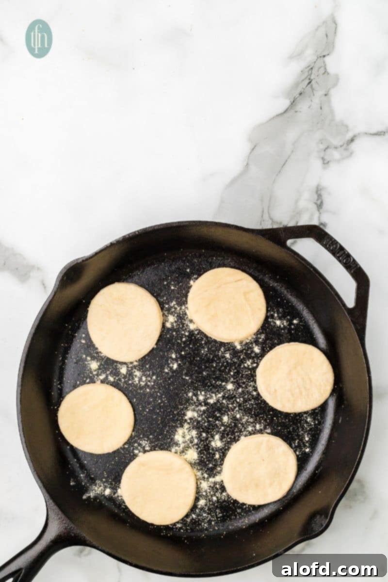 Artisan Sourdough English Muffin Bread 19 A skillet sprinkled with flour, now holding 6 round doughs, beginning to cook.