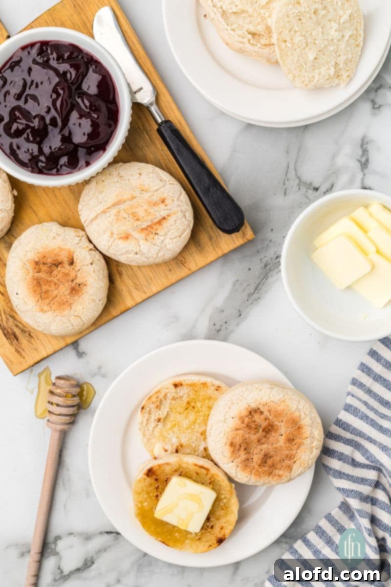 Artisan Sourdough English Muffin Bread 4 A charming scene featuring a plate of English muffins with butter, alongside a wooden platter piled with more muffins and a bowl of vibrant jam.