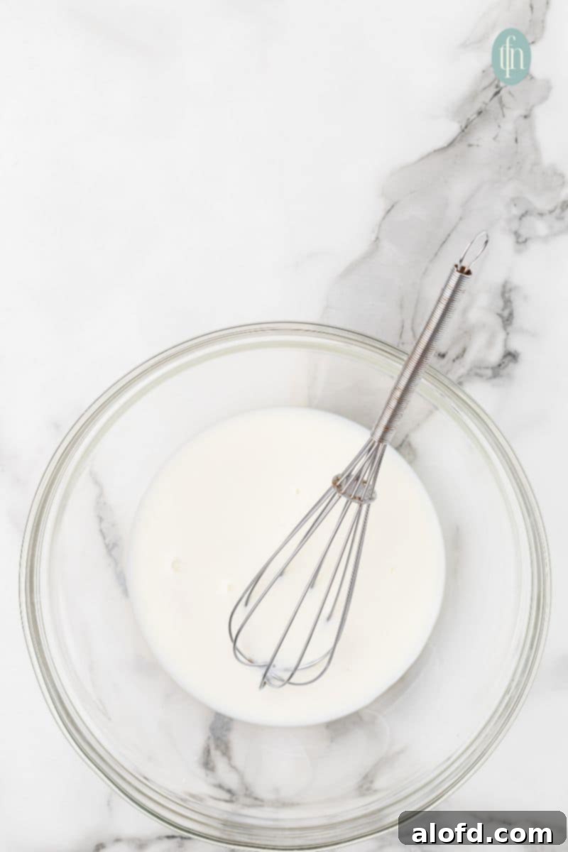 Artisan Sourdough English Muffin Bread 8 A clear mixing bowl showing a smooth, white liquid mixture after whisking the initial ingredients.