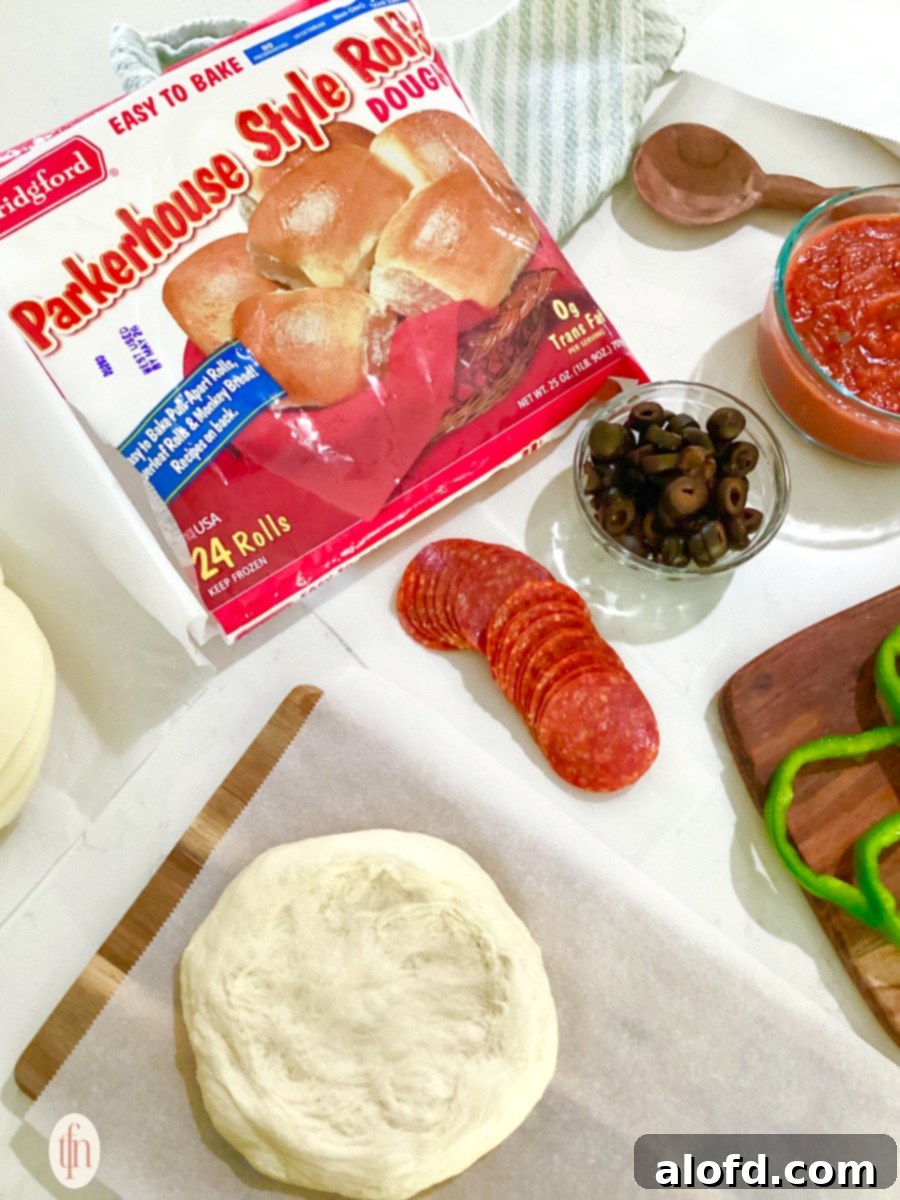 Monster Mash Pizza 5 A bag of Parkerhouse Style Roll dough is prominently featured on a countertop surrounded by pizza ingredients like pepperoni, olives, and a small round of dough on parchment paper.