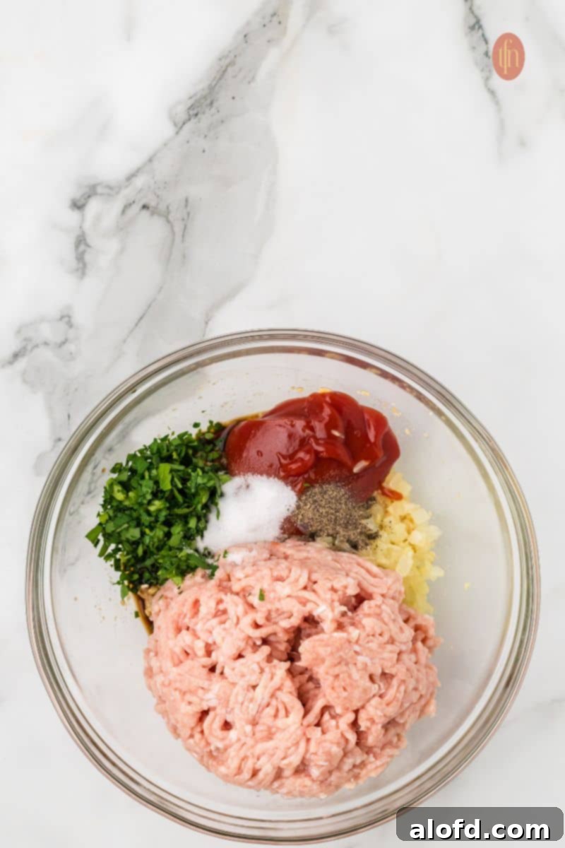Savory Chicken Meatloaf 11 A close-up, overhead shot of the chicken meatloaf ingredients in the mixing bowl before being combined, showing the ground chicken, parsley, seasoning, and sauce components.