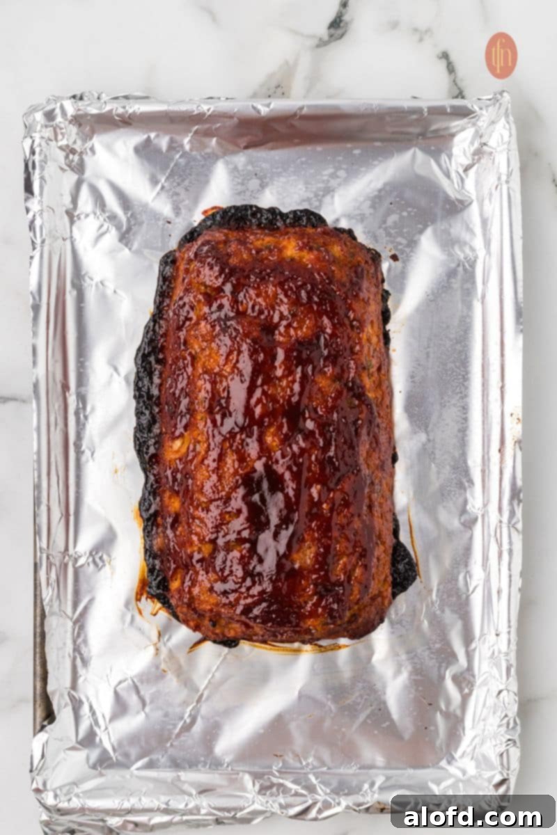 Savory Chicken Meatloaf 15 An overhead shot of the fully baked chicken meatloaf on the foil-lined baking sheet, covered in a glossy, dark red glaze.