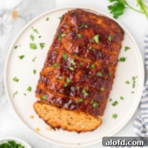 Savory Chicken Meatloaf 18 A square, overhead shot of a whole chicken meatloaf on a round white platter. It is already sliced and topped with a glossy glaze and chopped parsley.