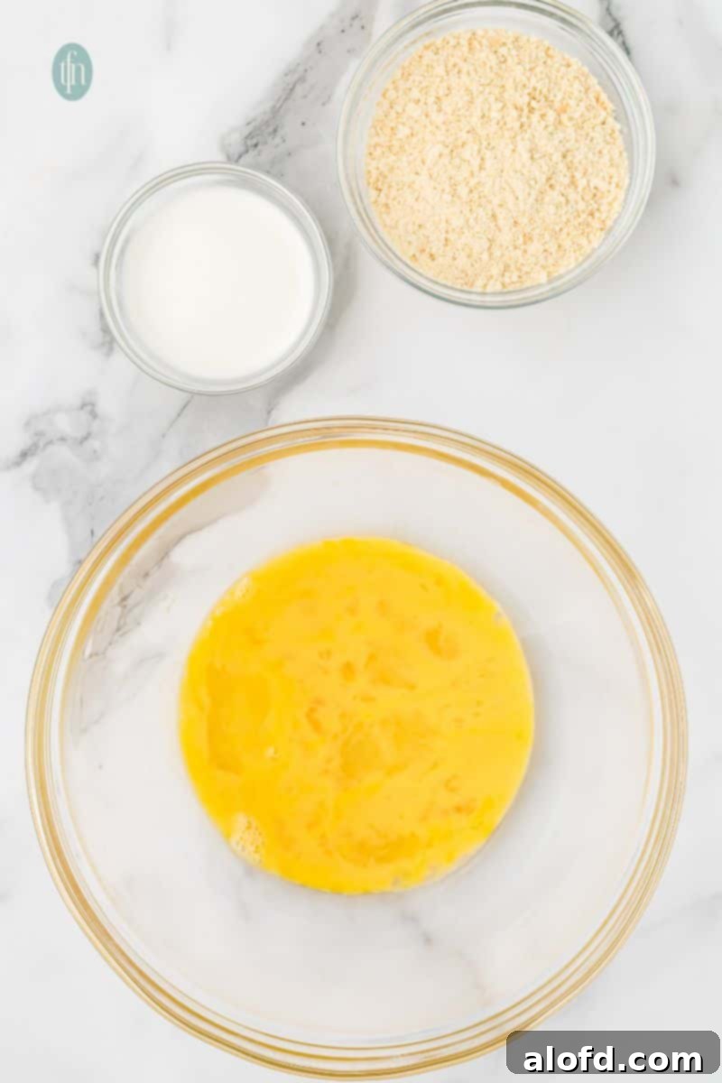 Savory Chicken Meatloaf 7 A large glass mixing bowl contains whisked eggs. Two small bowls are above it, one with milk and another with breadcrumbs.