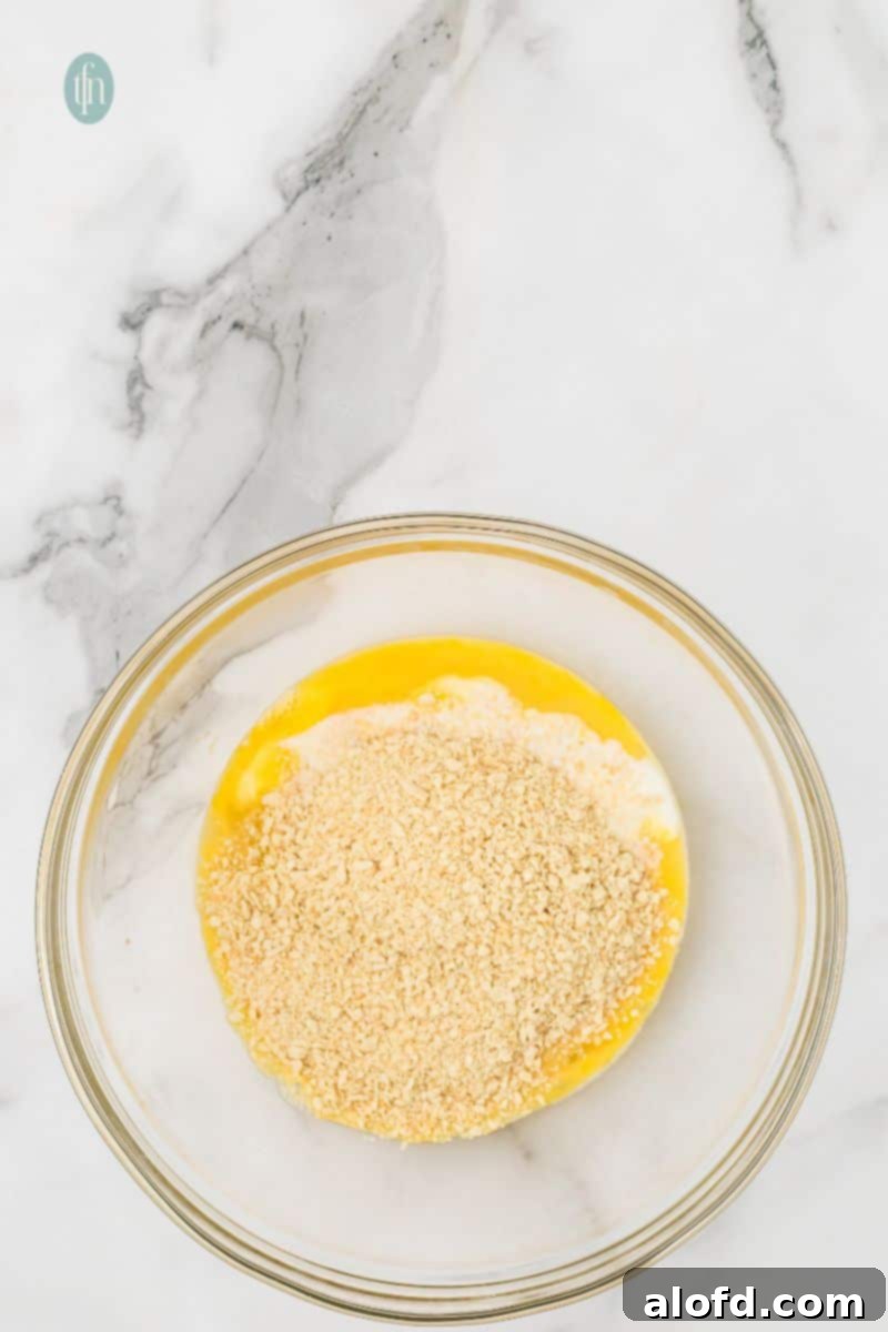 Savory Chicken Meatloaf 8 An overhead shot of a large glass bowl containing whisked eggs and milk, topped with a layer of dry breadcrumbs.