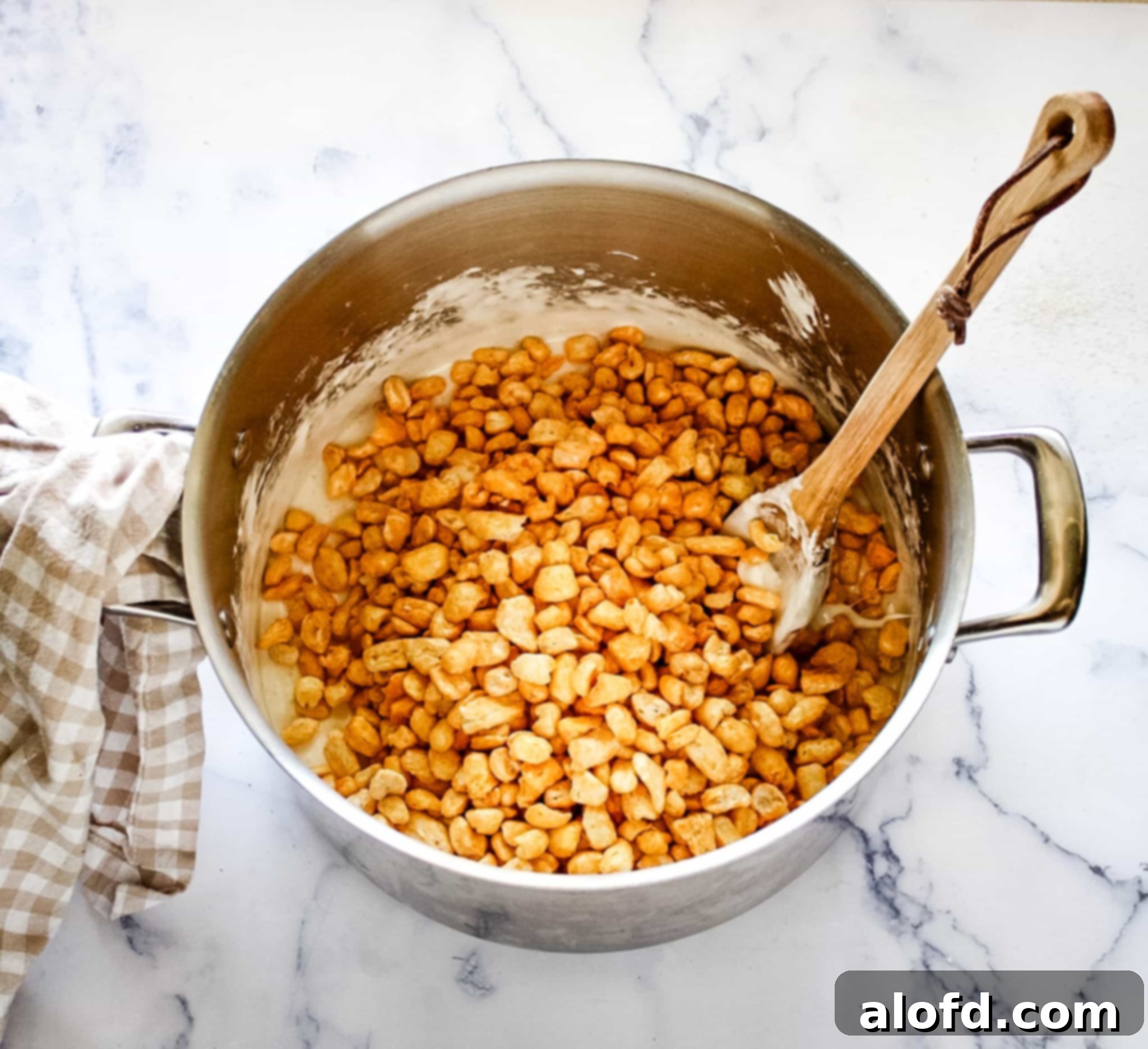 Golden Corn Pops cereal being mixed into melted butter and marshmallows in a large silver pot, creating a gooey mixture.