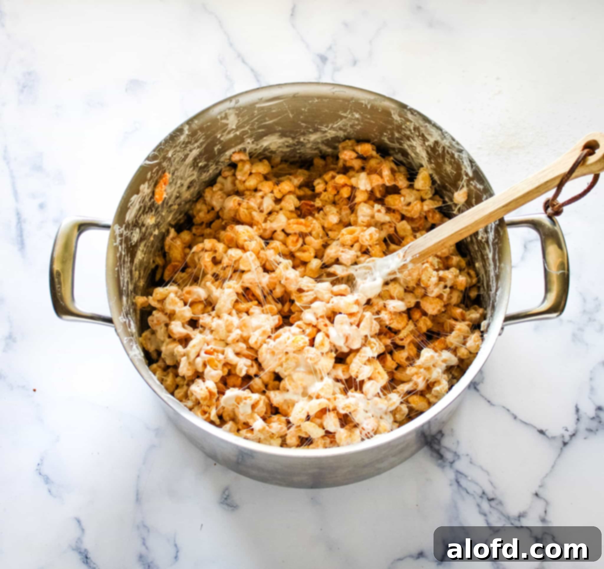 A spatula lifting a spoonful of the warm, sticky Corn Pops and marshmallow mixture from a pot, showcasing the perfect texture for shaping cereal treats.