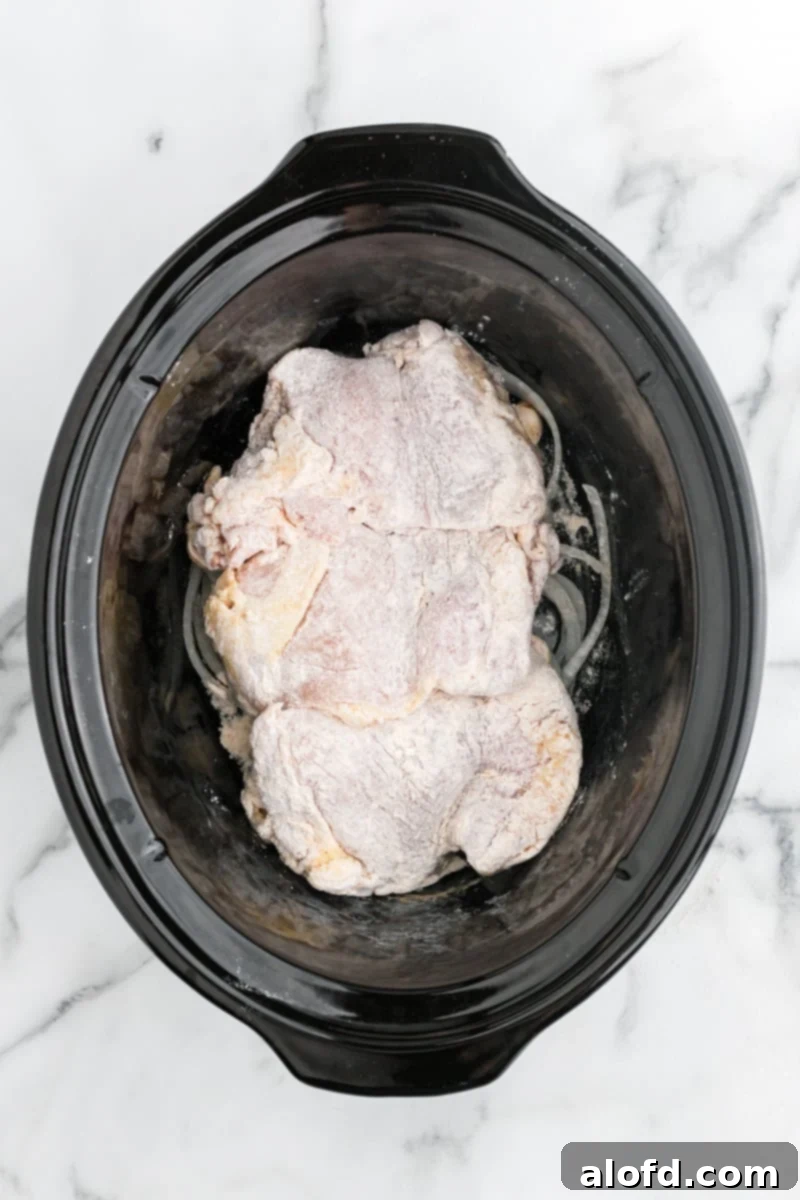 Comforting Crockpot Smothered Chicken 6 Chicken thighs layered over sliced onions in a crock pot, ready for cooking.