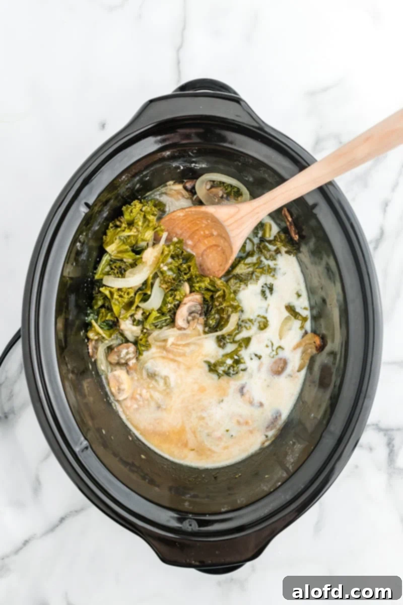 Comforting Crockpot Smothered Chicken 9 Creamy chicken gravy and a wooden spoon with other ingredients in a crockpot, ready to be stirred.