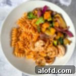 a white plate of Blackstone Vegetables with pasta and shrimp.
