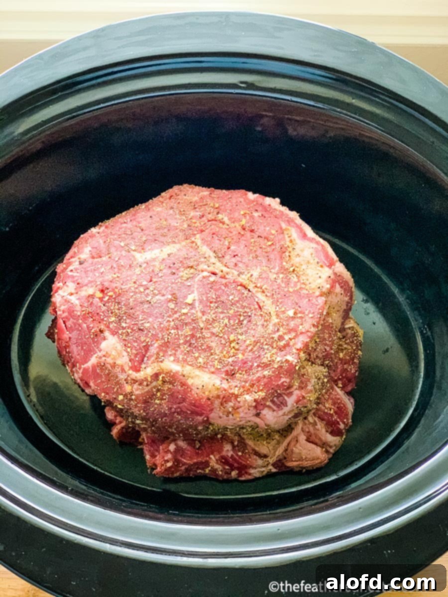 Fall-Apart Slow Cooker Pot Roast 3 Close-up of a beef chuck roast seasoned and ready to be placed in a slow cooker, with a sliced onion in the background.