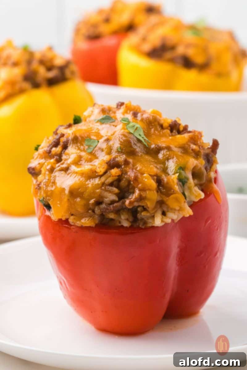 Loaded Taco Peppers 2 An eye-level shot of a single baked red taco stuffed pepper on a white plate, with the top of a yellow pepper visible in the blurred background. This dish is a perfect blend of comfort and flavor, showcasing the vibrant colors and appealing texture of the filling.