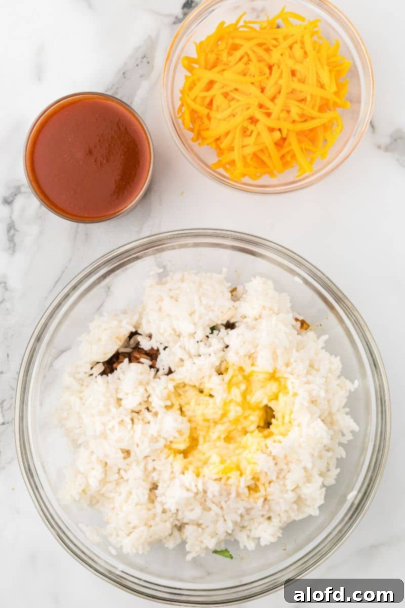 Loaded Taco Peppers 10 A glass bowl of the ground beef and rice mixture has melted butter poured over the rice, adding richness. A bowl of shredded cheddar cheese and a bowl of enchilada sauce are positioned next to it, awaiting incorporation.