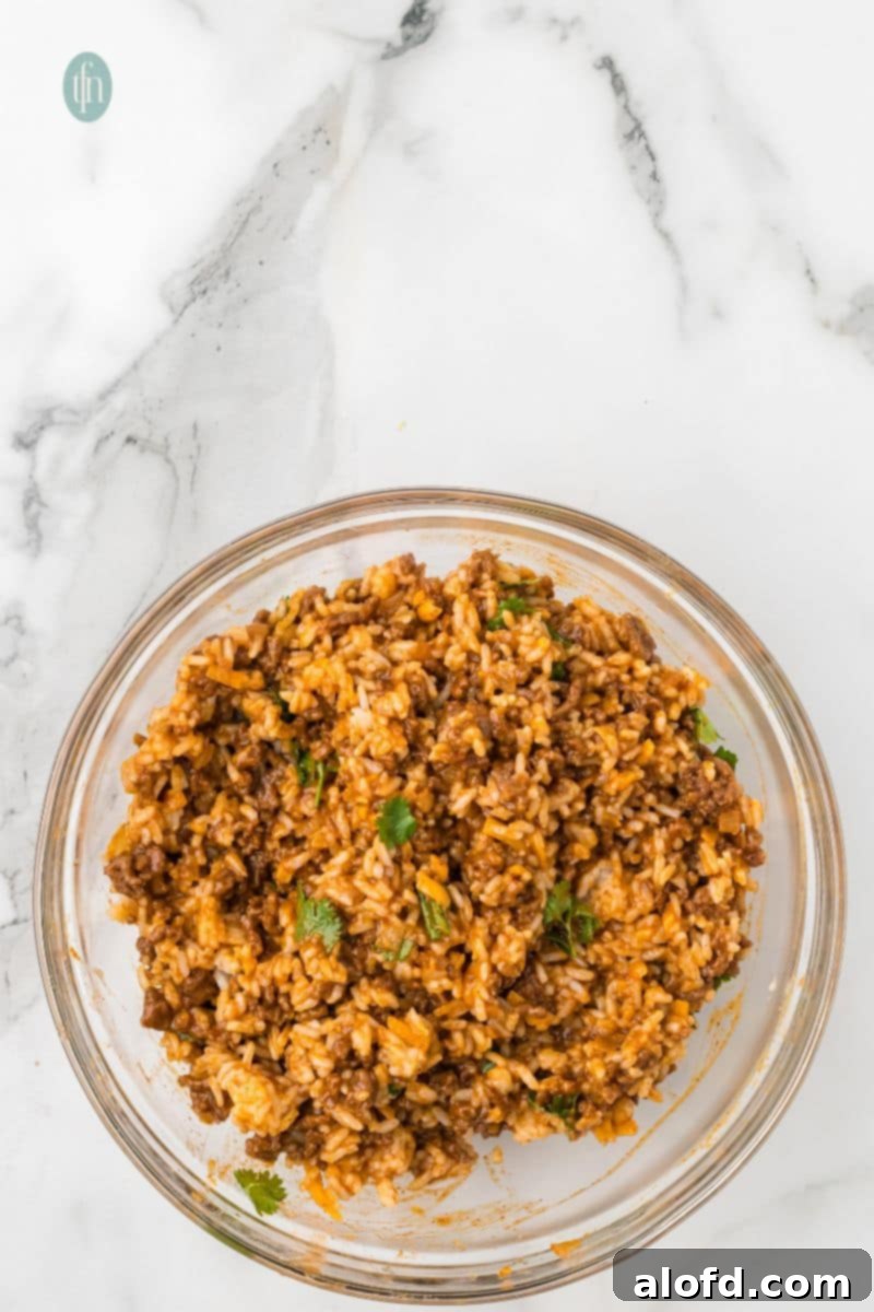Loaded Taco Peppers 11 A large glass mixing bowl holds the finished stuffing mixture—a perfectly combined blend of seasoned ground beef, rice, melted cheese, and rich sauce, now ready to generously fill the prepared bell peppers.