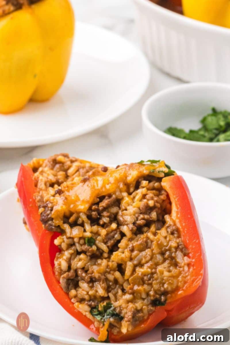 Loaded Taco Peppers 15 A close-up shot of a red stuffed bell pepper half cut open on a white plate, revealing the rich, cheesy, ground beef and rice filling. The vibrant colors and textures make this dish incredibly appetizing.