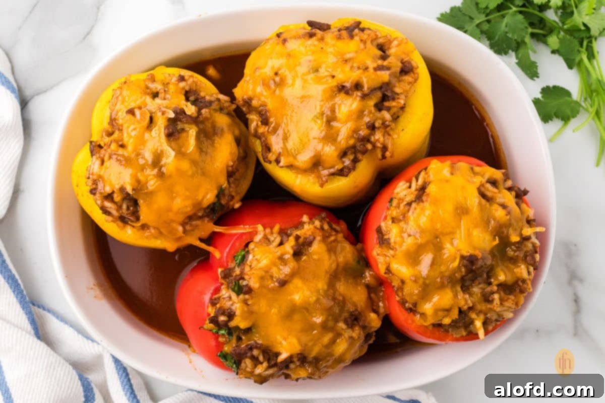 Loaded Taco Peppers 17 An overhead shot of four baked taco stuffed peppers (two red and two yellow) in a white oval baking dish. The peppers are filled with a cheesy, meat and rice mixture, and are sitting in a rich red sauce, ready to be served.