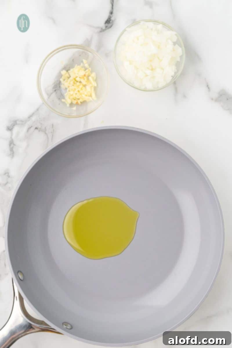 Loaded Taco Peppers 6 An overhead shot of a gray nonstick pan with a pool of olive oil. Small glass bowls of chopped garlic and diced onion are visible on the marble counter above the pan, ready for sautéing.
