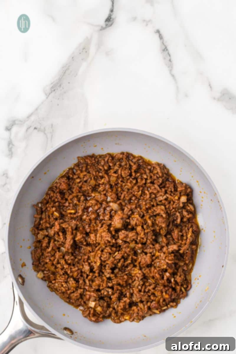 Loaded Taco Peppers 8 A close-up, overhead view of seasoned ground beef mixed with onions and garlic, perfectly cooked and browned in a gray nonstick pan, forming the savory base of the taco filling.