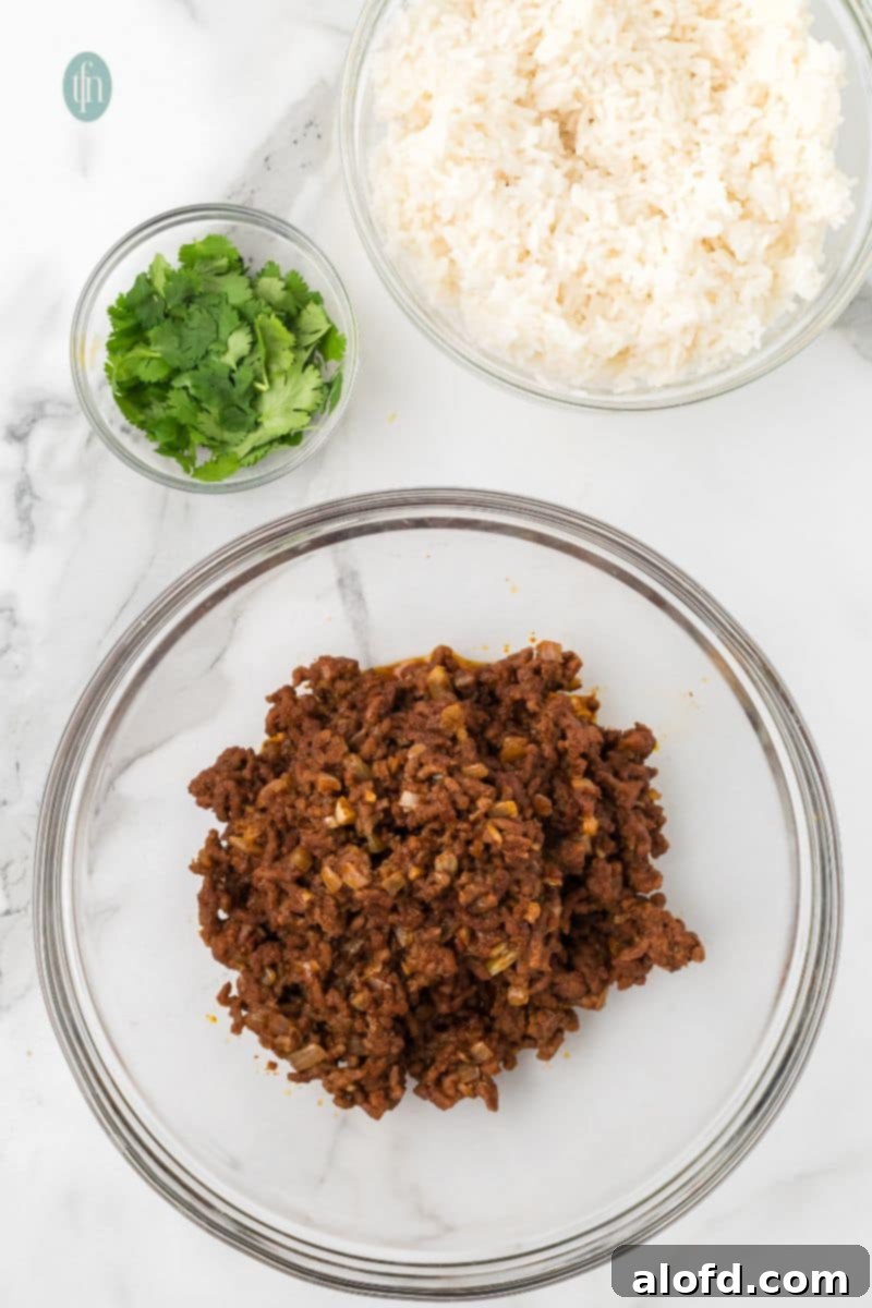 Loaded Taco Peppers 9 Cooked and seasoned ground beef is in a large glass mixing bowl, ready for the next steps. Other ingredients, including bowls of cooked white rice and chopped cilantro, are on the counter, poised to be added to the mixture.