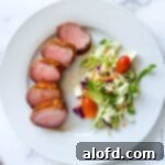 Slices of smoked pork tenderloin on a white dinner plate with a side salad.