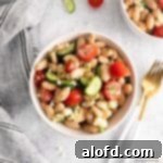 a white bowl of tuscan bean salad with silverware to the right and a striped napkin on the left with the corner of another bowl of white bean salad showing on the top right.