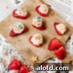 Strawberries topped with cream and sprinkles on a wooden board.