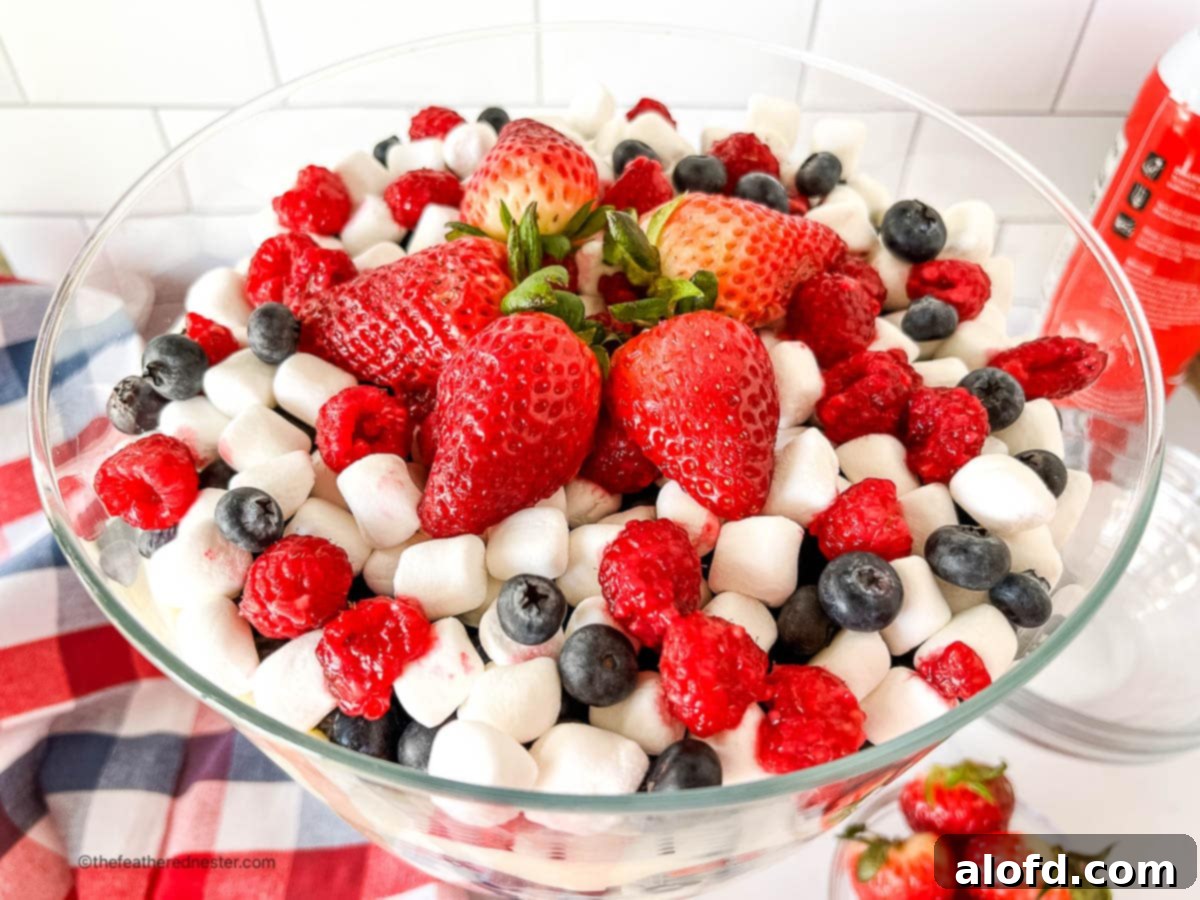 Patriotic red, white, and blue 4th of July salad in a large elegant glass serving bowl, showcasing layers of fruit and cream.