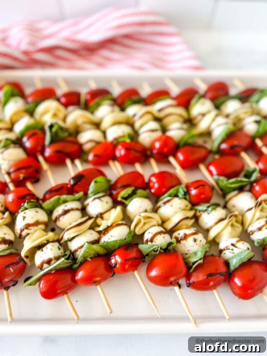 A white tray of colorful tortellini skewers with a balsamic glaze on top, placed on a festive red and white napkin.