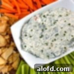 Knorr spinach dip on a serving rectangular bowl. Served on top of a round wooden board with crackers and vegetables.