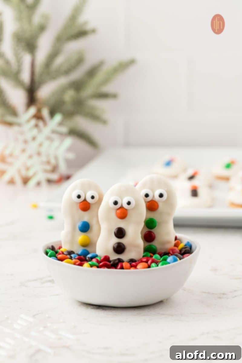 Top 10 Holiday Cookie Delights 14 Three decorated Nutter Butter snowman cookies with a Christmas tree decoration in the background.
