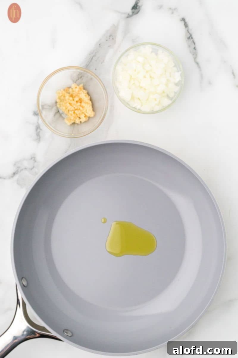 Olive oil heating in a skillet, with a bowl of chopped onion and minced garlic.