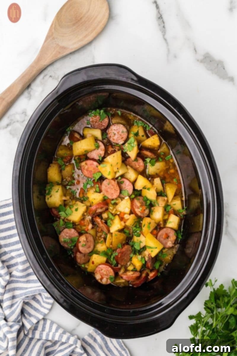 Slow-Cooker Sausage and Potato Delight 2 Crockpot filled with cubed potatoes, sausage, onion, bell peppers, garlic, and spices.