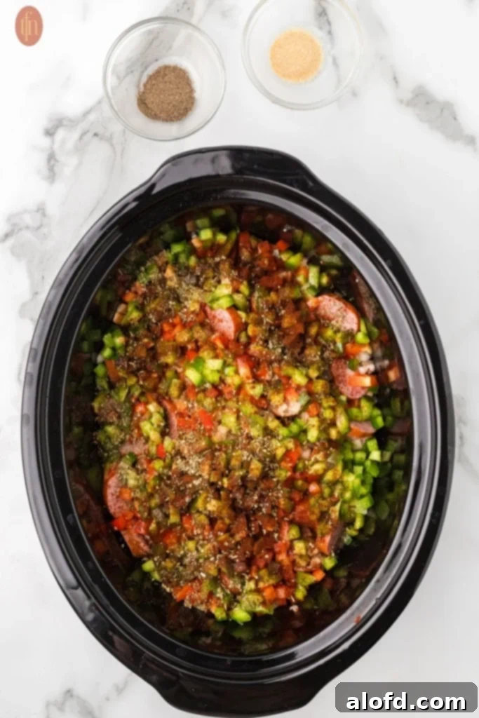 Slow-Cooker Sausage and Potato Delight 10 Crockpot with potatoes, sausage, onions, bell peppers, and garlic, with spices above it.