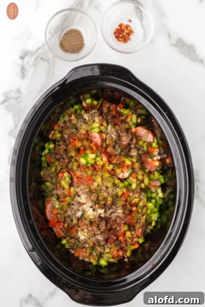 Slow-Cooker Sausage and Potato Delight 11 Crockpot with potatoes, sausage, onions, bell peppers, and garlic, with spices above it.