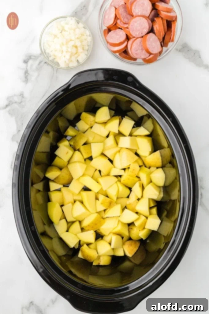 Slow-Cooker Sausage and Potato Delight 5 Crockpot full of cubed potatoes with sausage and onions next to it.