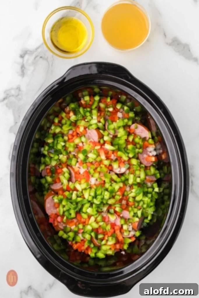 Slow-Cooker Sausage and Potato Delight 7 Crockpot with potatoes, sausage, onions, bell peppers, and garlic, with broth and oil next to it.