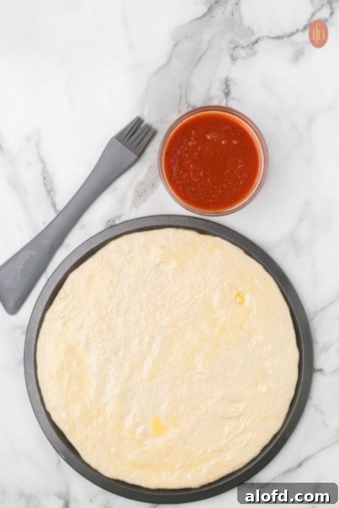 Homemade Pizza with a Crust Made from Scratch 8 Pizza dough in a pan with marinara sauce.