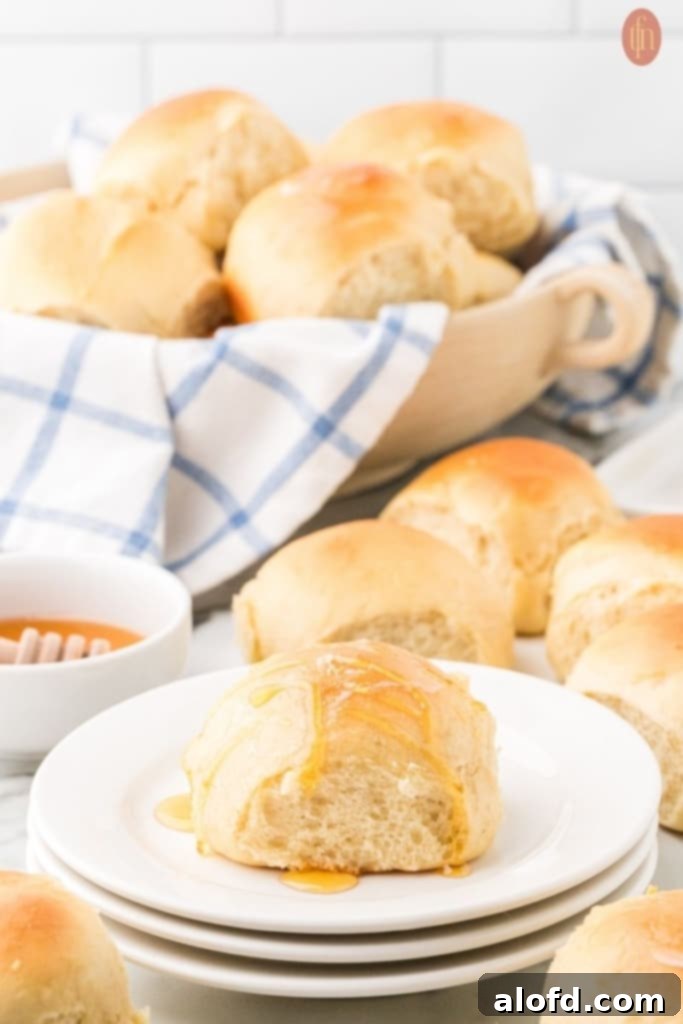 Quick Dinner Rolls 14 A plate of dinner rolls and more rolls in the background, resting on a wooden bowl with a blue and white checkered cloth.